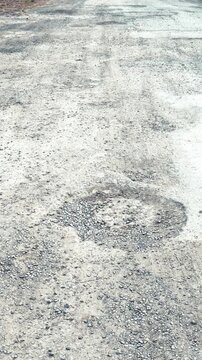 Worn asphalt road with pothole, daylight rural surface showing circular crater and loose gravel, desolate empty street