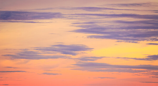 Beautiful vibrant twilight sky background with colorful pastel purple grey and golden orange clouds at sunset for inspirational nature wallpaper panorama