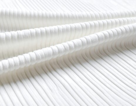 Close-up of a textured white ribbed fabric, displaying soft folds and linear patterns with a gentle light highlighting the ridges