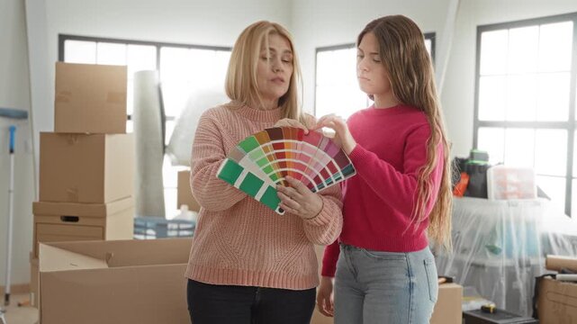 Two women hold a paint palette while daughter points finger at swatches in a building with moving boxes and covered furniture; renovation planning concern.