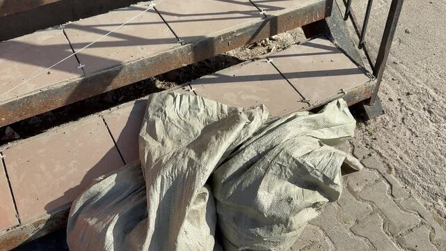 Porch steps with cracked tiles and exposed mortar, sunlight casting railing shadows across surface, installer prepping substrate