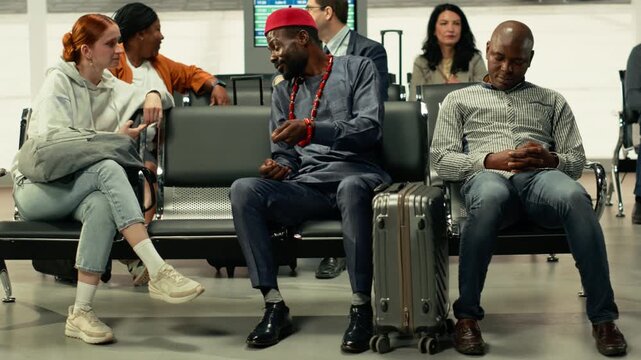 Man in traditional African clothing and woman waiting at bus station, couple traveling via interstate coach. Passengers monitor timetable screen departure board while preparing bags, migration.