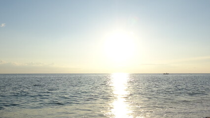 Obraz premium Bright Sunrise over the Horizon with Distant Boat on the Sea. High-angle glowing sun reflecting on the ocean surface with a tiny boat visible on the distant horizon during early morning.