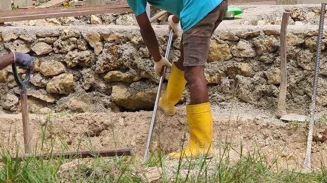 Close-up footage of a construction worker digging a trench at a building site, wearing yellow safety boots. Ideal for infrastructure, labor, engineering, and construction industry concepts.