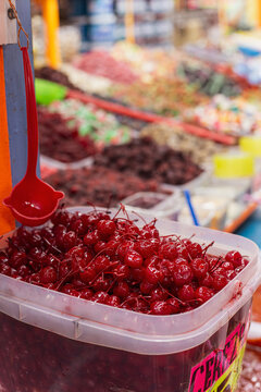 Cerezas en alm&iacute;bar en recipiente para venta en granel y cuchar&oacute;n rojo para servir