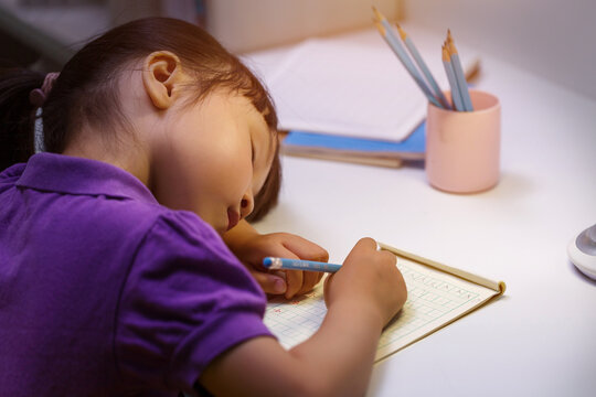 Exhausted little girl sleeping on desk while doing homework or studying at night