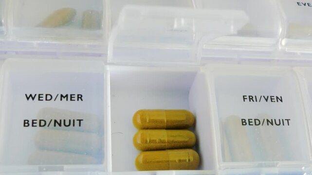 Weekly pill organizer box with brown capsules in open compartment