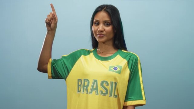 Woman points finger upward in studio wearing yellow green brasil jersey with brazil flag patch and bold brasil lettering; national pride.