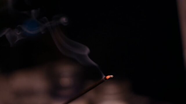 Burning incense with smoke in a dark or dim setting.
