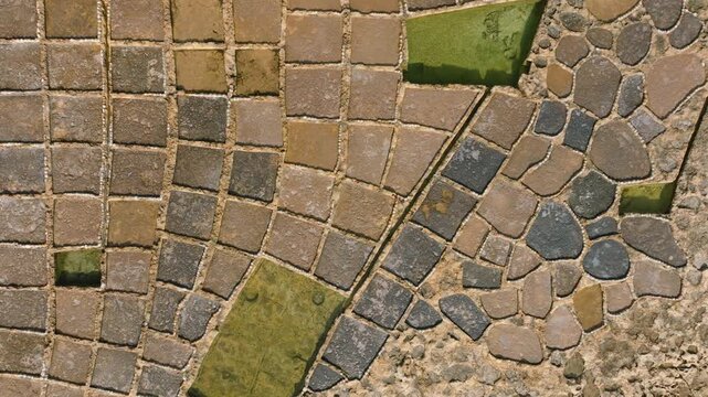 Top-down drone tracking movement over salt pans on Gozo Malta with lateral parallel motion. camera remains fixed vertically downward, revealing a continuous geometric grid of rectangular salt basins 
