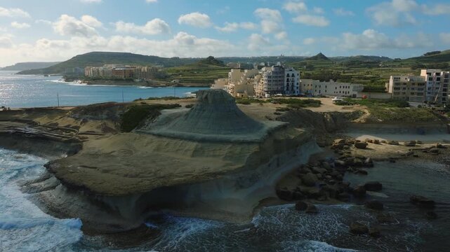 Cinematic aerial drone flight over Qolla l-Bajda limestone formation on Gozo Malta coastline. shot reveals a pale, sculpted rocky hill rising above surrounding coastal terrain, shaped natural erosion