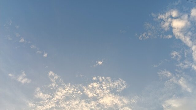 Landscape photo capturing small, scattered white clouds clearing up on a soft blue afternoon sky.
