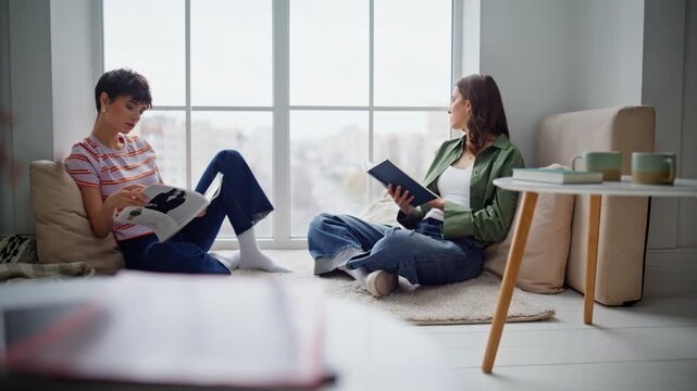 Relaxed two readers sitting light apartment floor. Couple women reading home