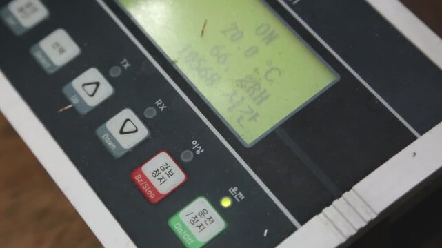 실내 공조 제어 시스템 패널 LCD 디스플레이 잔상 디테일 자재: 실내 훈련장 공조 제어기의 연두색 LCD 화면에 투영된 ON, OFF 텍스트 잔상과 초록색 운전 LED 불빛, 물리 버튼 조작부를 사선에서 타이트하게 포착한 익스트림 클로즈업 영상입니다. 빌딩 관리 시스템, BMS, 인터페이스, 기계 메커니즘 및 산업 테크놀로지 콘셉트의 정밀한 인서트 숏을 