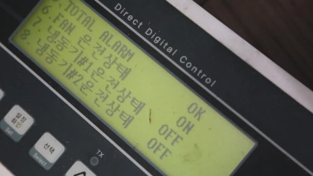 실내 공조 제어 시스템 디지털 패널 LCD 디스플레이 자재: 빌딩 관리 및 실내 환경 모니터링을 위한 직접 디지털 제어기 패널의 연두색 LCD 화면에 표시된 온도, 습도, 운전 시간 텍스트와 수치를 사선에서 포착한 익스트림 클로즈업 영상입니다. 설정 버튼을 담았으며 공조 시스템, BMS, 에너지 관리 및 스마트 빌딩 콘셉트의 정밀한 인서트 숏을 상징합니다.