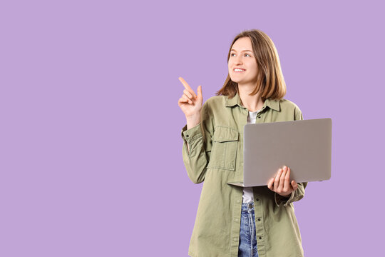 Happy female programmer with laptop pointing at something on purple background