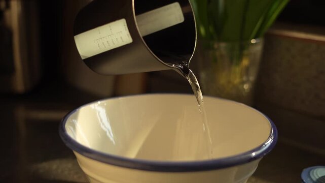 Pouring water from a black measuring jug into a white bowl