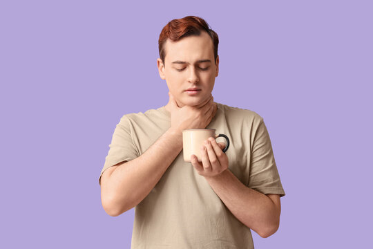 Young man with sore throat and hot tea on lilac background