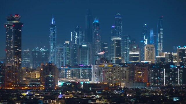 Dubai cityscape glows at night with towering skyscrapers and modern architecture. Residential villas in foreground contrast with illuminated high-rise buildings against deep blue sky.
