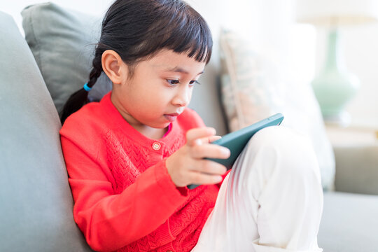 Smiling child staring at mobile device while resting on couch