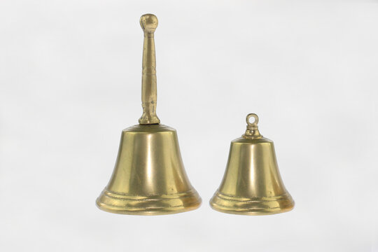 Golden bells gleam against a clean white background. One bell stands tall, the other smaller, rounded. Both feature classic brass finish with polished surfaces. Decorative vintage metal gold bell set 