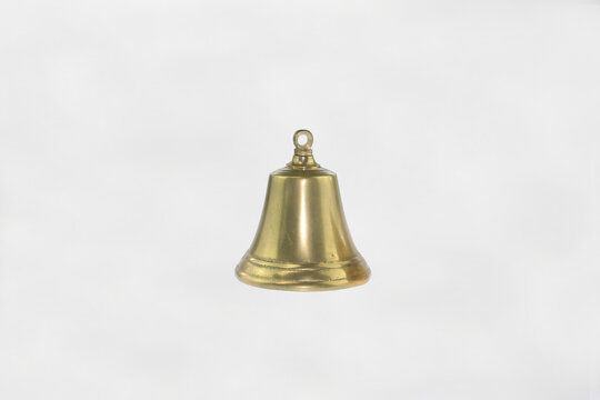 Small brass bell hangs against clean white background. Polished surface gleams with soft golden tones. Simple form evokes tradition and quiet alertness. Minimalist metal bell golden brass texture 