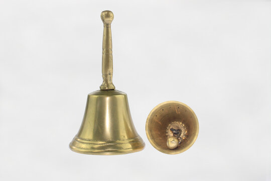 Golden bell with elegant handle stands upright. Its hollow interior reveals worn, decorative centerpiece. Simple white backdrop highlights object's vintage craftsmanship, decorative traditional metal 