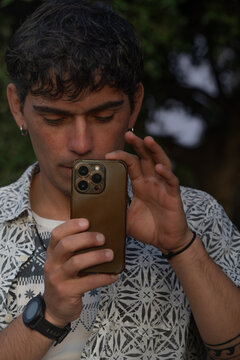 Retrato de un joven con pendientes y un tatuaje tomando una fotograf&iacute;a con su tel&eacute;fono m&oacute;vil.