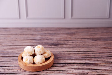 Fototapeta premium Kue Salju Soft, powdered treats rest in a wooden bowl. Warm wood grain adds rustic charm. Minimalist background emphasizes sweet delicacy. Gentle lighting enhances inviting texture. Ideal for food 