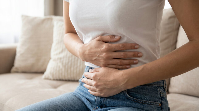 Young woman on couch holding abdomen symbolizing stomach pain, period cramps, and wellness care.