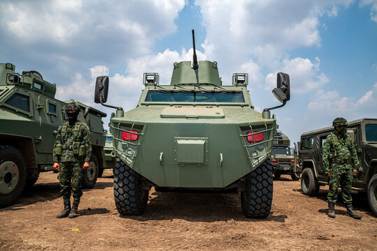 Front view of a green military armored personnel carrier (APC) with soldiers in camouflage uniforms standing guard during outdoor tactical training operations.