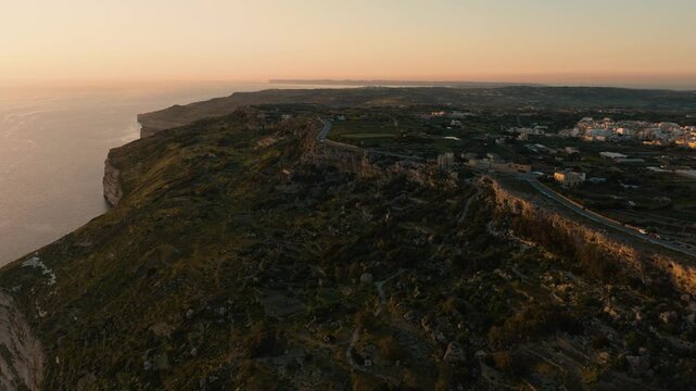 Aerial drone flight along Dingli Cliffs, Malta at sunset with dramatic coastal escarpment, Mediterranean horizon and last golden light on limestone coastline