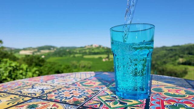 Slow Motion Pouring Sparkling Water into Blue Glass on Mosaic Table