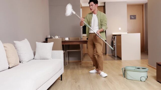Joyful young man guy listening music and washing floor use mop dancing singing having fun while cleaning apartment, household housekeeping in positive mood, domestic work, householding, cleans house