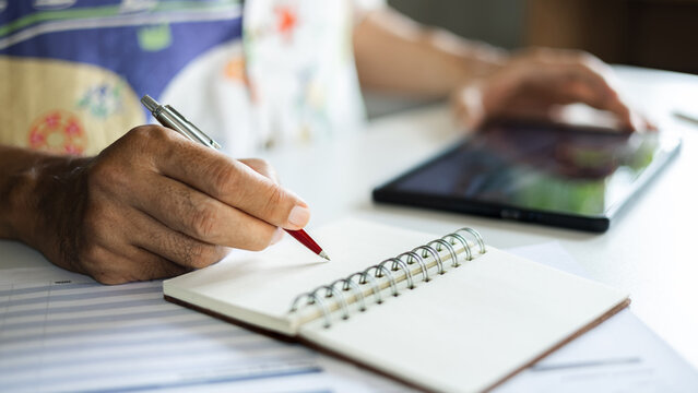 close-up shot, casual man working at home taking note and using wireless technology to start new business online, E-commerce via digital tablet