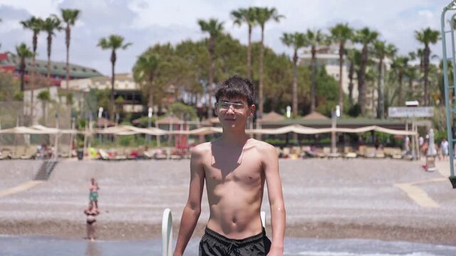 Young vacationer in swim shorts walking near seaside resort after swimming during sunny summer holiday. Young tourist enjoys sunny weather on summer holiday at seaside.