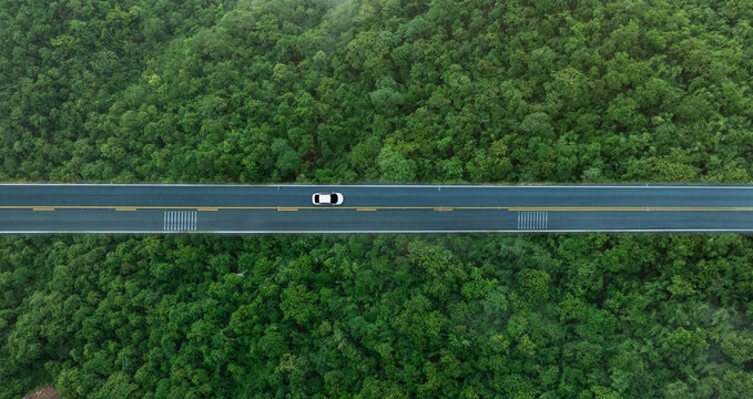 Aerial view of dark green forest road and white electric car Natural landscape and elevated roads Adventure travel and transportation and environmental protection concept	