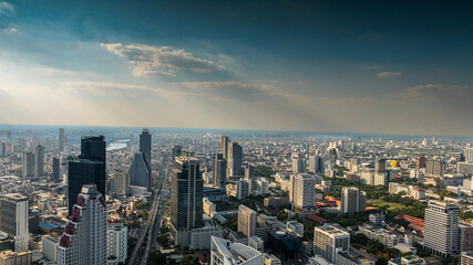 Obraz premium Panoramic aerial view of Bangkok city skyline featuring modern skyscrapers, dense urban buildings, and dramatic cloudy sky during daytime. Metropolitan cityscape of Thailand with business district arc