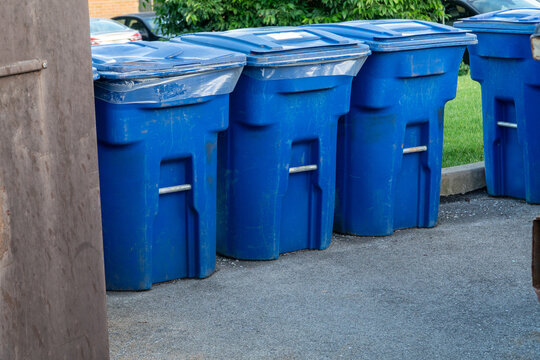 Row of weathered blue plastic recycling bins lined up on an asphalt street for curbside collection, symbolizing environmental responsibility and waste management in a residential area.