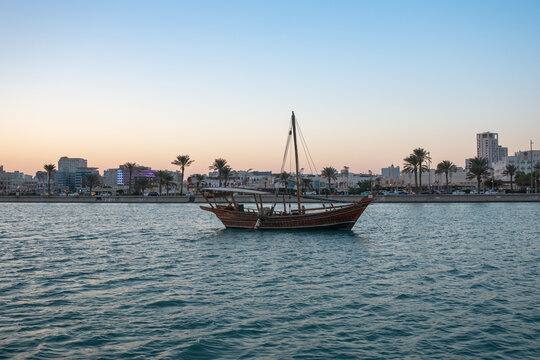 Traditional wooden boat on water with city skyline in background.