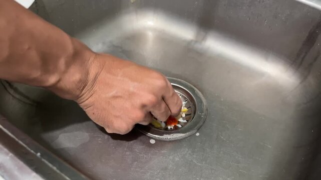 Close Up View of Man Hand Lifting and Cleaning Food Waste Strainer Plug from Stainless Steel Kitchen Sink