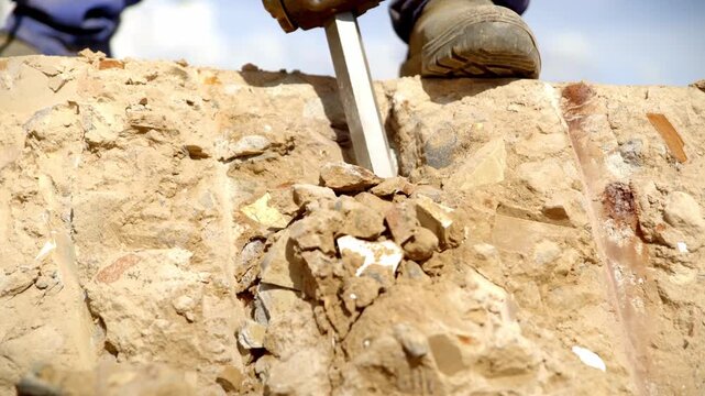 Close-up of a construction worker using a hydraulic hammer drill to break rock and concrete at a demolition and construction site. Industrial machinery performing heavy-duty excavation work outdoors.
