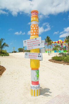 Directional signage in Cococay&rsquo;s scenery glows: white sand beaches curve into turquoise water, palm trees sway, and coral reefs shimmer below. Hills roll green behind the shore