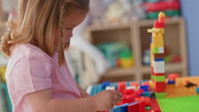 Little girl holding a toy block and building a tall colorful tower with hands in a building; concentration creativity.