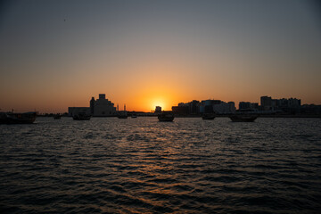 Fototapeta premium Sunset over a city skyline with boats on the water.