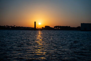 Fototapeta premium Sunset over water with silhouette of landscape in background.