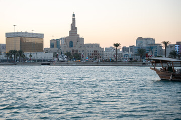 Fototapeta premium Cityscape at dusk with modern buildings and a traditional wooden boat on the water.