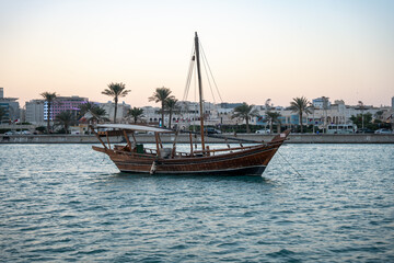Obraz premium Traditional wooden boat on water with city buildings and palm trees in background.
