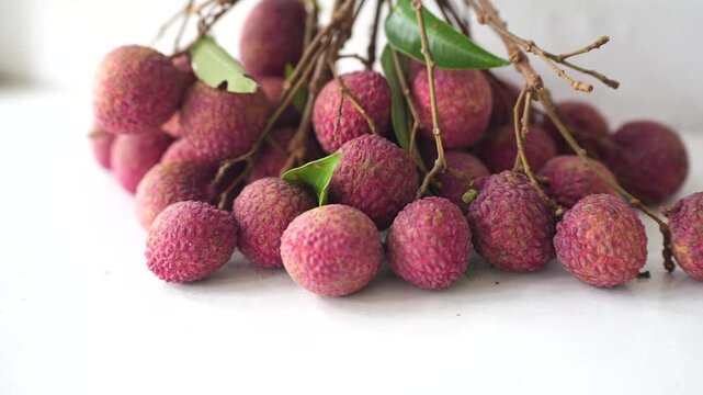 Fresh pink lychees clustered with natural branches and green leaves, showcasing a tropical fruit harvest with vibrant texture.