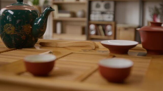 Close up no people shot of teapot with elegant gold-painted designs on wooden board, surrounded by tools and clay cups for tea ceremony